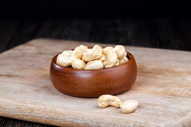 Cashew nuts on an old wooden table and in a wooden bowl, close-up of a large number of cashew nuts on a table and on a wooden surface in a wooden plate