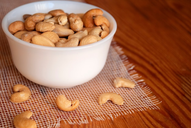 Cashew nuts in a white bowl on a wooden table.