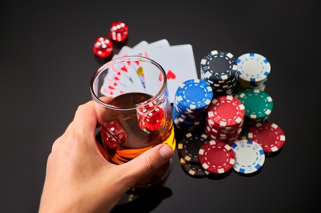 Casino chips playing cards glass of whiskey and dices on dark reflective background