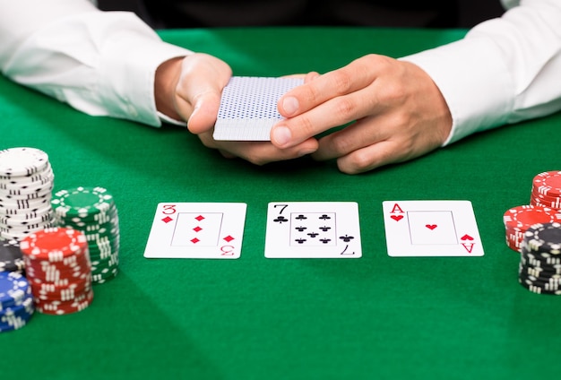 casino, gambling, poker, people and entertainment concept - close up of holdem dealer with playing cards and chips on green table