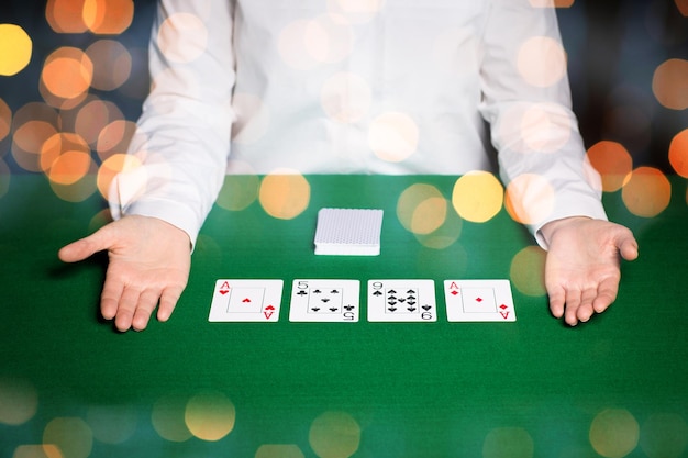 casino, gambling, poker, people and entertainment concept - close up of holdem dealer with playing cards on green table over holidays lights background