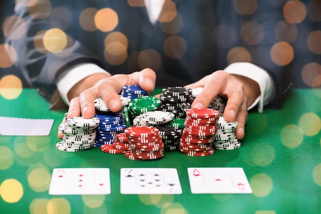 casino, gambling, poker, people and entertainment concept - close up of poker player with playing cards and chips at green casino table over holidays lights background