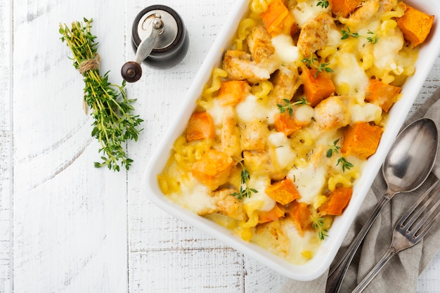 Casserole from chicken meat, pumpkin, pasta ,thyme, cheese and bechamel sauce in ceramic form on light concrete or stone table. Selective focus. Top view. Copy space.