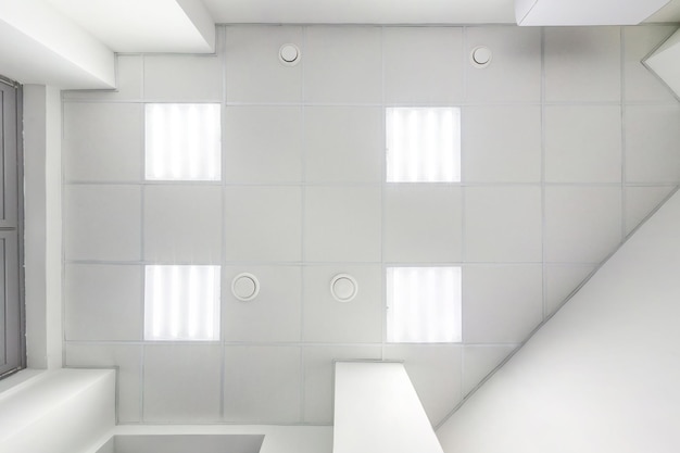 Cassette suspended ceiling with square halogen spots lamps and drywall construction in empty room in apartment or house Stretch ceiling white and complex shape Looking up view