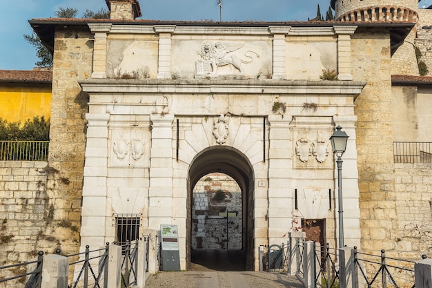 Castello di Brescia. The entrance of the medieval fortress with the lion sculpture. The castle has towers, a trench, a bridge made of white marble stones, bricks, in an Italian city Brescia, Lombardy