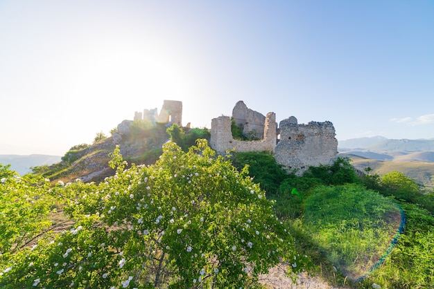 Castle ruins on mountain top at Rocca Calascio, italian travel destination, landmark in the Gran Sasso National Park, Abruzzo, Italy. Clear blue sky sun burst in backlight