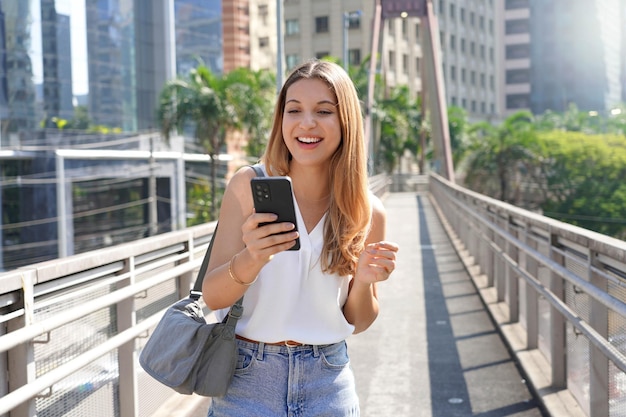 Casual attractive Brazilian woman watching her smartphone walking in the morning on footbridge in the metropolis of Sao Paulo Brazil