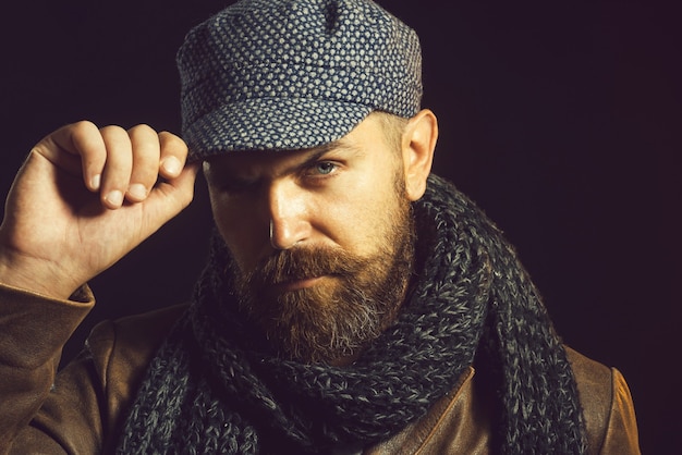 Casual bearded male in jacket gray scarf and cap on head male fashion bearded hipster adjusting his