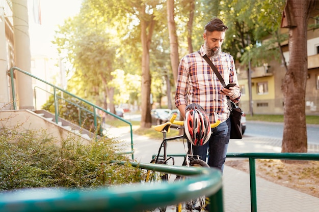 Casual businessman going to work by bicycle. He is pushing bike and sending text message.