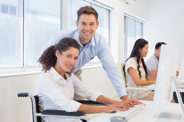 Casual businesswoman in wheelchair working at her desk with colleague