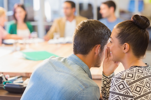 Casual businesswoman whispering secret to her colleague