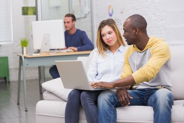 Casual colleagues using laptop on couch in office