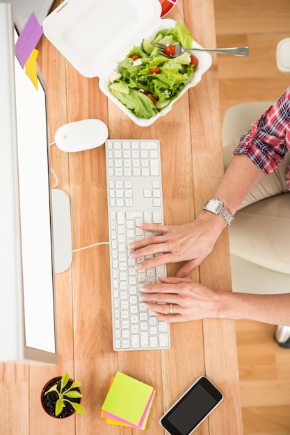 Casual designer working with computer and eating salad