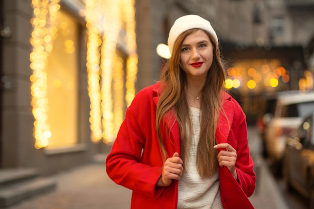 Casual dressed blond woman in white hat and winter coat walking at the city. Space for text