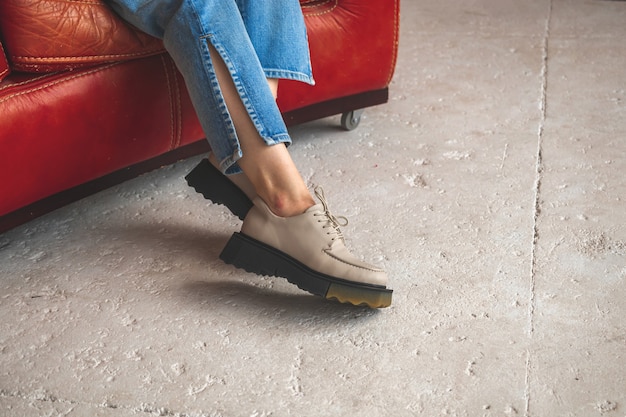 Casual fashion with urban shoes on female legs in denim jeans. Studio shot on red old leather chair and concrete background photo