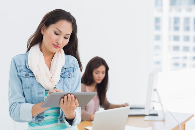 Casual female artist using digital tablet with colleague in background