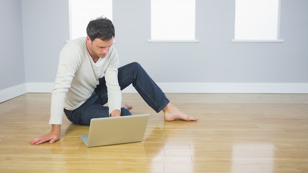 Casual handsome man sitting on floor using laptop