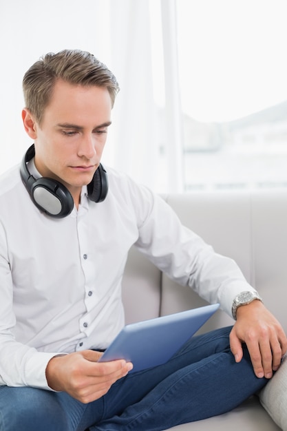 Casual serious young man using digital tablet on sofa