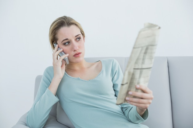 Casual thinking woman phoning while sitting on couch