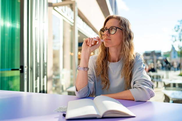 Casual woman sitting at table and taking notes in notebook on the cafe terrace