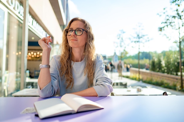 Casual woman sitting at table and taking notes in notebook on the cafe terrace