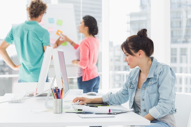 Casual woman using computer with colleagues behind in office