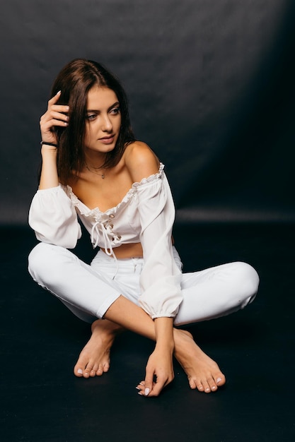 Casual woman on white clothes sitting on the floor over black background Provence concept