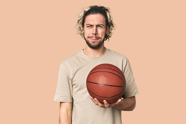 Casual young basketball player in studio confused feels doubtful and unsure