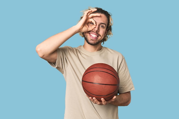 Casual young basketball player in studio excited keeping ok gesture on eye