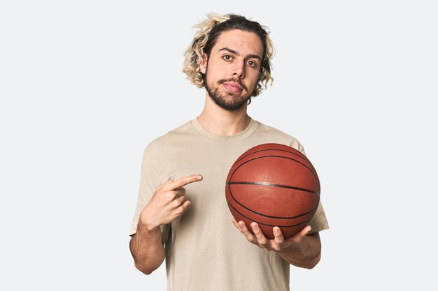 Casual young basketball player in studio smiling and pointing aside showing something at blank space