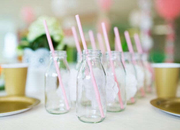 catering, dishware, holidays and celebration concept - closeup of glass bottles for drinks with straws on table