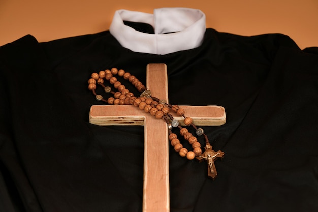 The Catholic cross and rosary lie on the black robe of the priest on a beige background