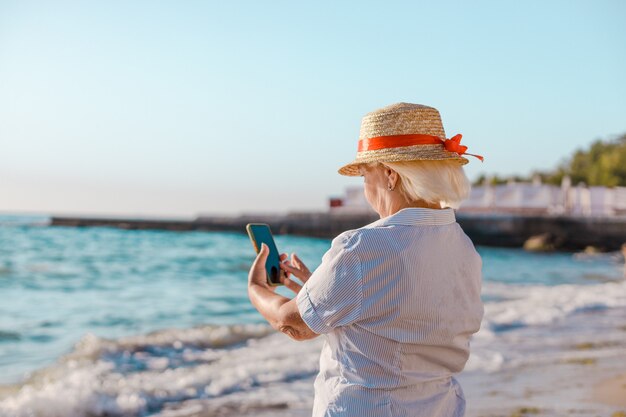 Caucasian blond woman in straw hat and striped shirt makes photo by smartphone