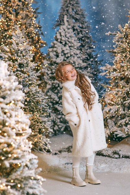 caucasian blonde girl in white eco fur coat walking in winter christmas forest with lights