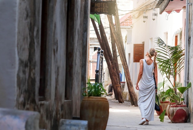 Caucasian blonde woman walking on the street of the old town with a long white dress