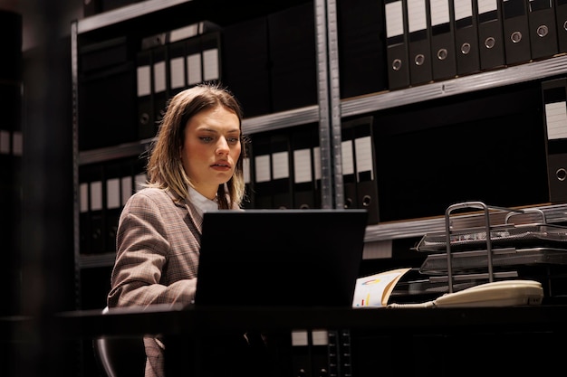 Caucasian bookkeeper reading administrative files, working late at night in corporate depository. Businesswoman in formal suit analyzing accountancy report, checking management research