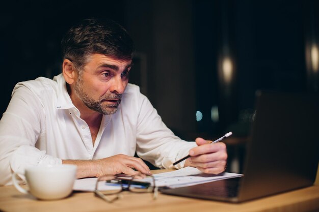 Caucasian boss working late sitting on desk in office at night Business man feeling tired and stress for overload jobxA