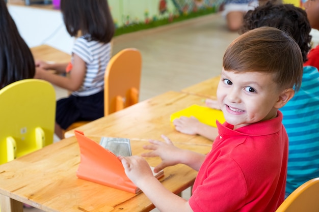 Caucasian boy ethnicity kid smiling in classroom with friends in kindergarten school.