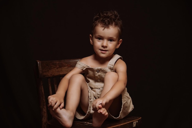 Caucasian boy in jumpsuits with a stylish hairstyle is sitting on a wooden chair