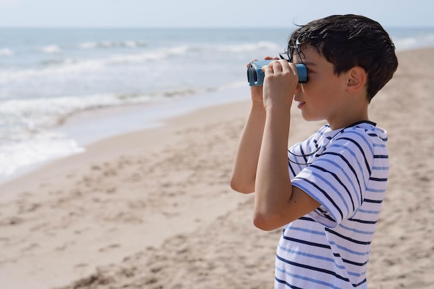 Caucasian boy looking through binoculars at the horizon on the beach in summertime