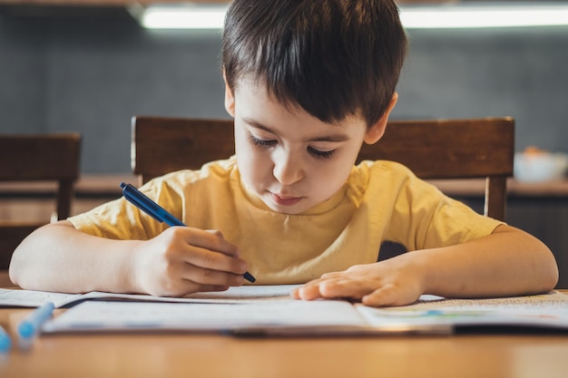 Caucasian boy studying at home writing notes sitting at desk front view distance education front vie...