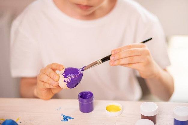 A Caucasian boy in a white tshirt paints eggs to celebrate the Easter holiday with bright colors