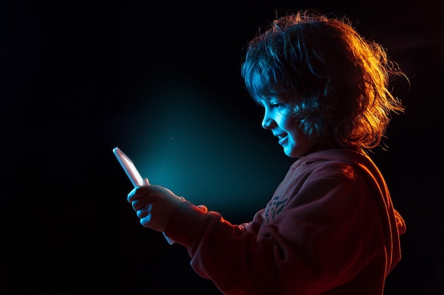 Caucasian boys portrait isolated on dark studio background in neon light