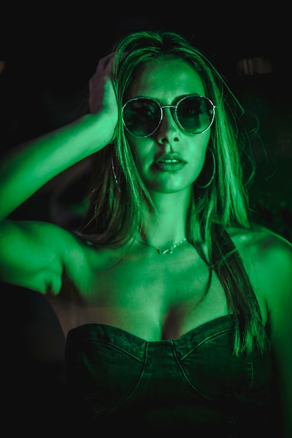 Caucasian brunette in a black dress illuminated by green led light reflected in black crystals. Urban night photography. woman with sunglasses