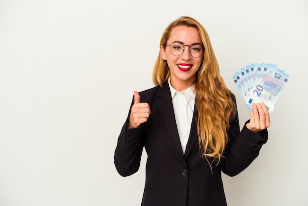 Caucasian business woman holding bills isolated on white background smiling and raising thumb up