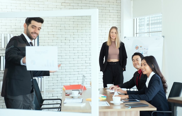 Caucasian business woman stand and look at coworker man giving presentation with multi ethnic team.