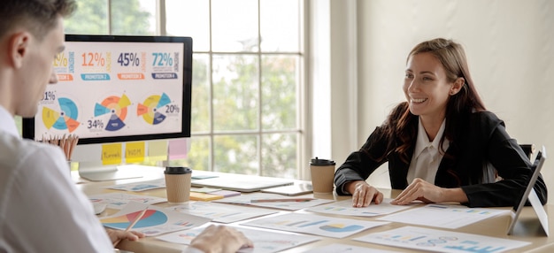 Caucasian businesswoman manager sitting smiling preparing explaining presenting analysis statistic financial data information report documents paperwork on desktop to businessman colleague in office.