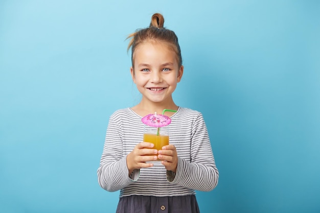 Caucasian child girl drinks orange juice and smiling Isolated studio portrait on blue background