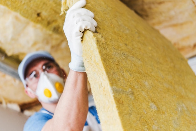 Photo caucasian construction worker with piece of insulating material roof insulating by mineral wool