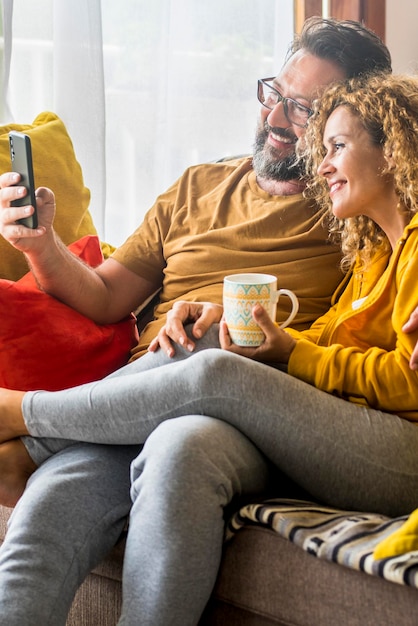 Caucasian couple doing video call with mobile phone at home sitting on the sofa Man and woman enjoying technology wireless connection during morning breakfast and have fun calling friends